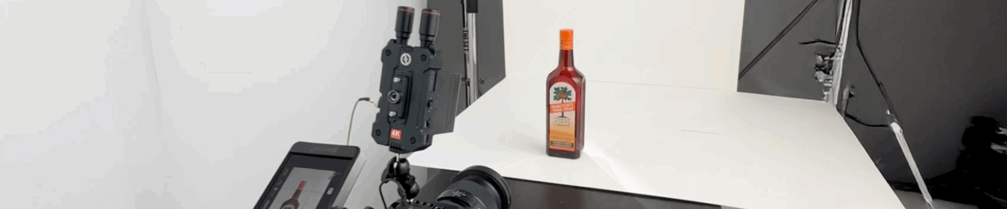 Behind-the-scenes photo shoot of a Munyon’s Paw-Paw liqueur bottle, with professional camera equipment aimed at the product on a white background.